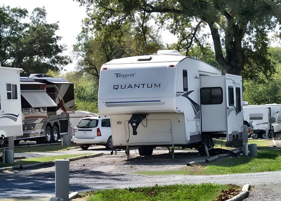 Fifth-wheel RV at a full-hookup site under the trees